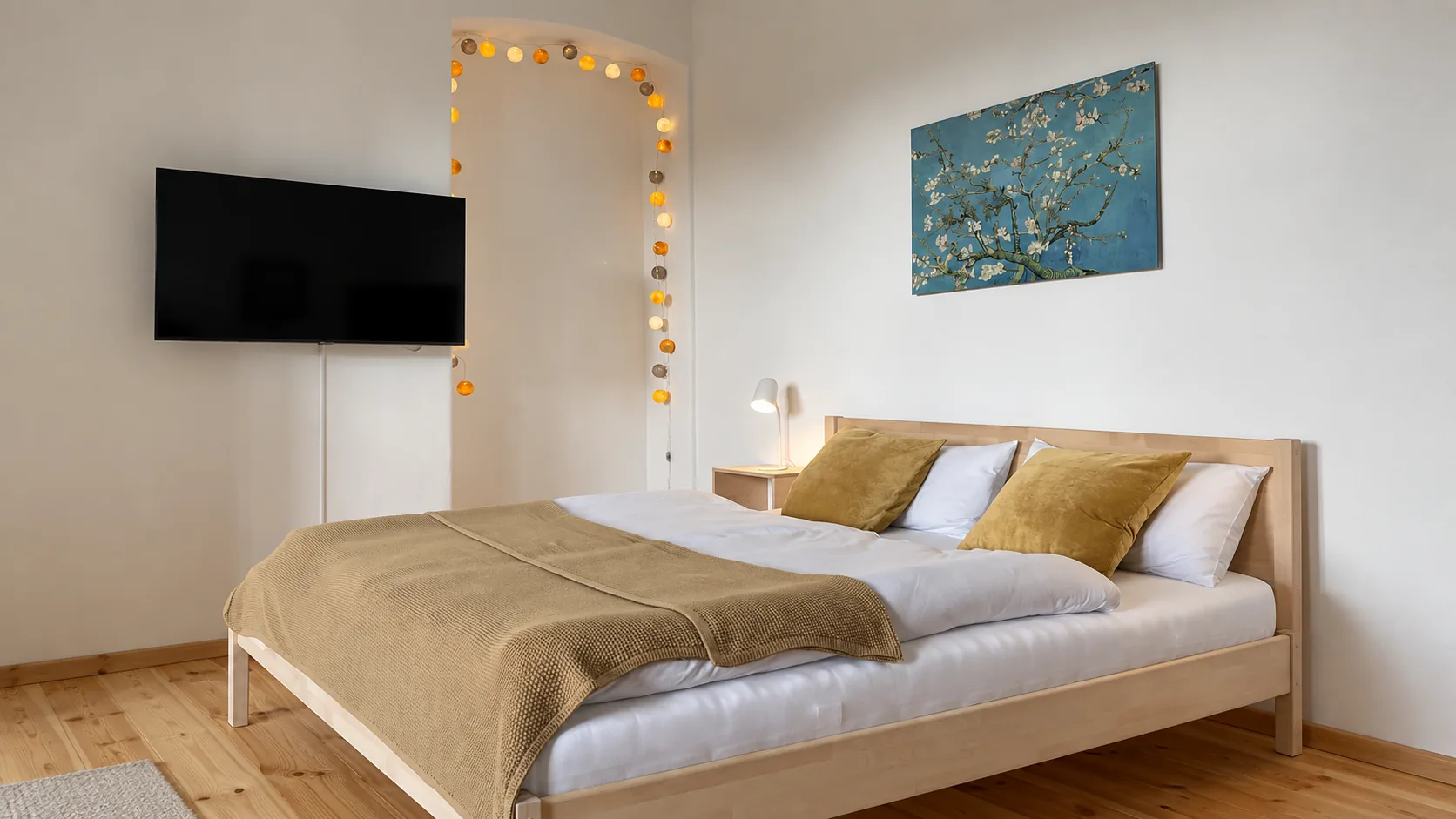 Schlafbereich mit Doppelbett, Lichterkette im Türbogen und Fernseher an der Wand